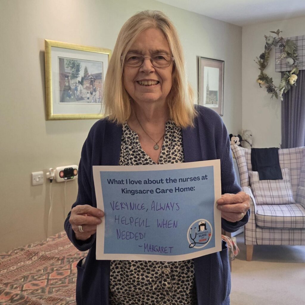 Resident holding up a sign that says: "What I love about the nurses at Kingsacre care home: Very Nice, always helpful when needed."