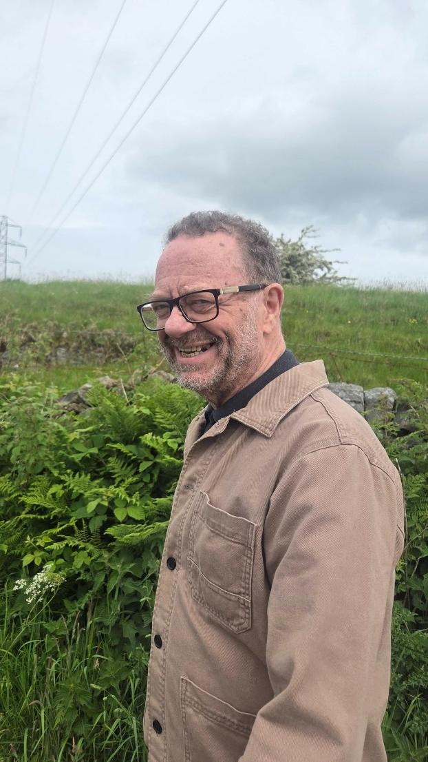 older man in a browwn jacket with glasses smiling at the camera
